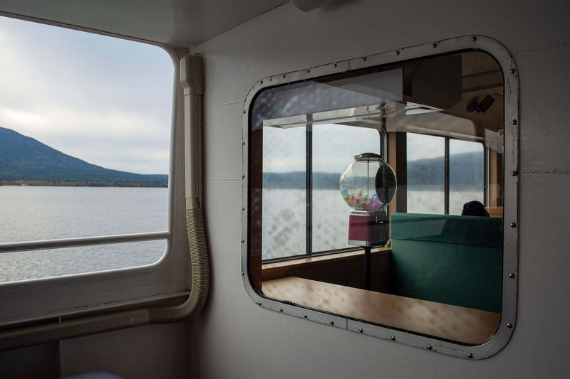Interior view from the Lake Akan sightseeing ferry showing a capsule toy machine and scenic lake reflection through the window.