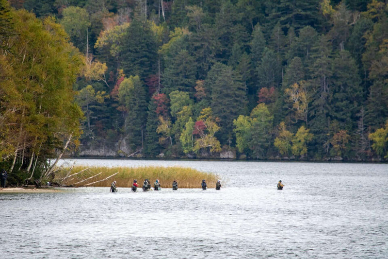 Ainu tribe members fishing in Lake Akan with vibrant autumn foliage in the background, showcasing traditional cultural practices in Hokkaido, Japan.