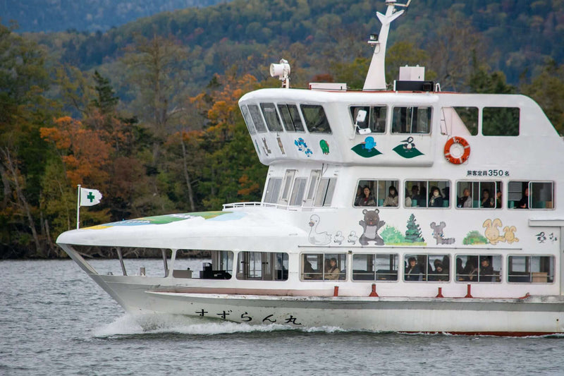 Lake Akan ferry with passengers and colorful cartoon characters, including a Marimo moss ball mascot.