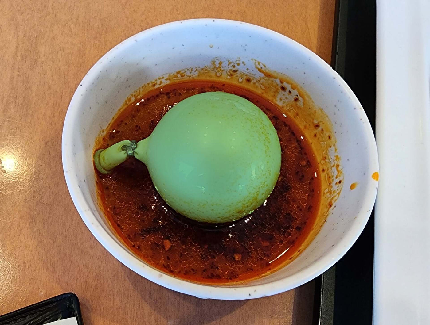 A marimo-inspired tofu dish served in the Lake Akan area, featuring a round green tofu ball resembling a marimo moss ball, placed in a bowl of savory chili-infused sauce.