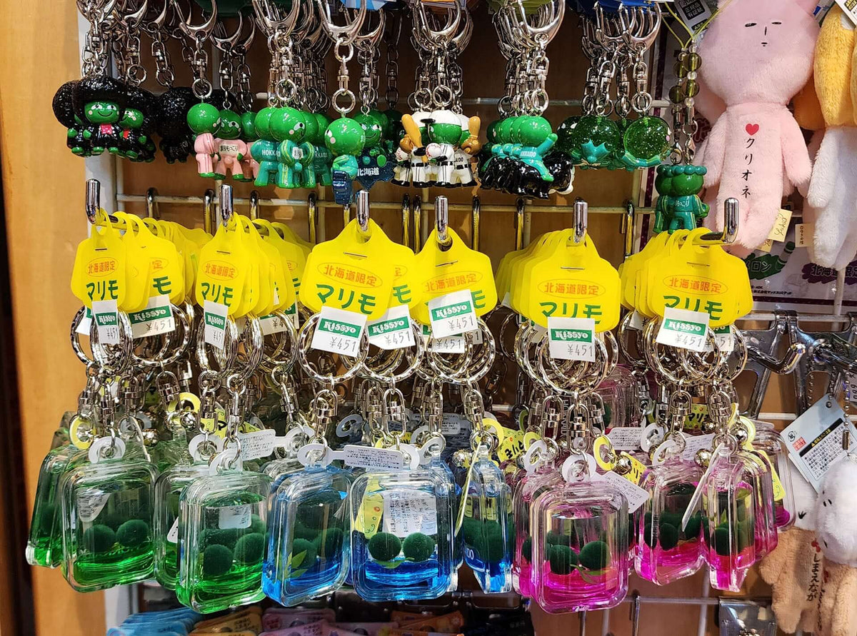 Display of faux marimo moss ball keychains and Marimokkori mascot keychains at a souvenir shop in Kushiro, Japan.