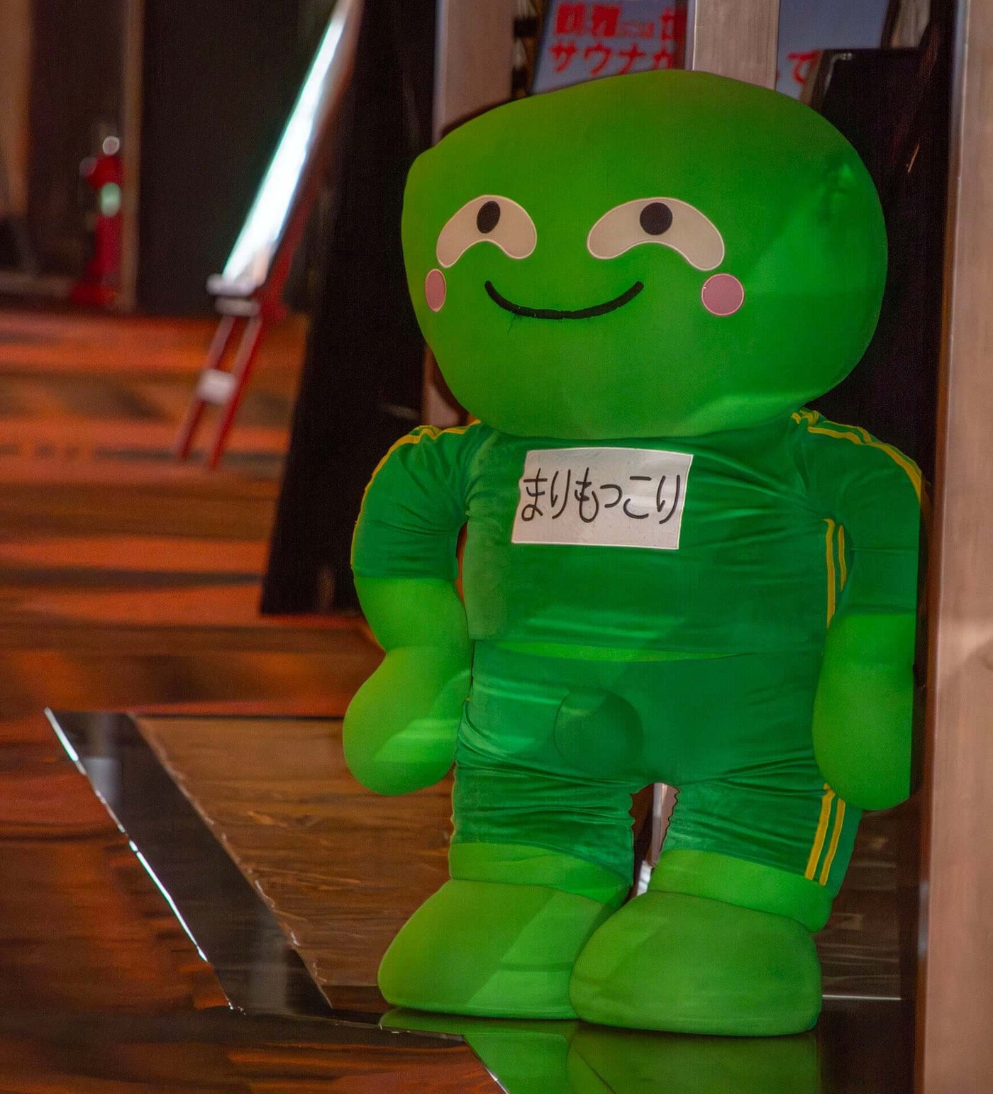 Life-sized plush figure of Marimokkori, the playful green mascot of Akanko Onsen, known for its round cheeks and exaggerated bulge.