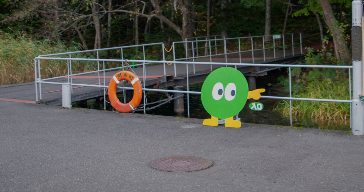 Churui Island dock at Lake Akan with Marimo mascot pointing toward the Marimo Exhibition Center.
