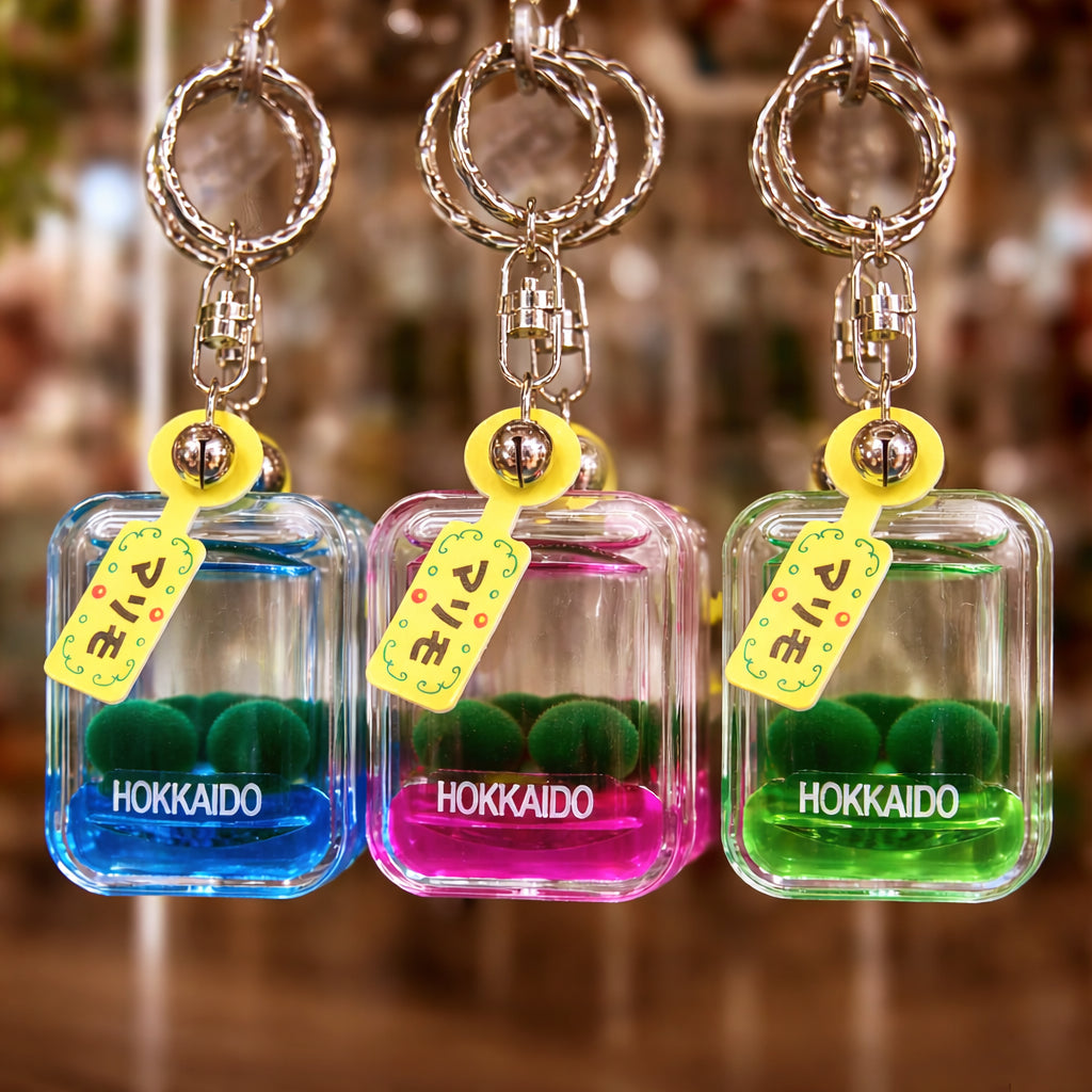 Marimo moss ball keychain trio in blue, pink, and green displayed on a souvenir rack in Lake Akan Hokkaido Japan