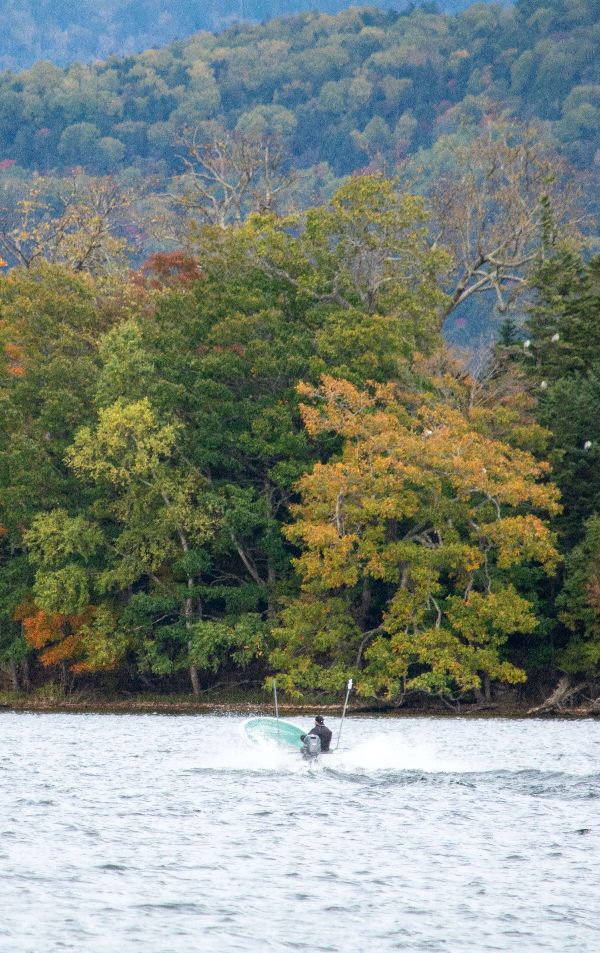 Small boat crossing Lake Akan in Hokkaido, Japan with vibrant fall foliage along the shoreline — home of the rare Marimo moss balls