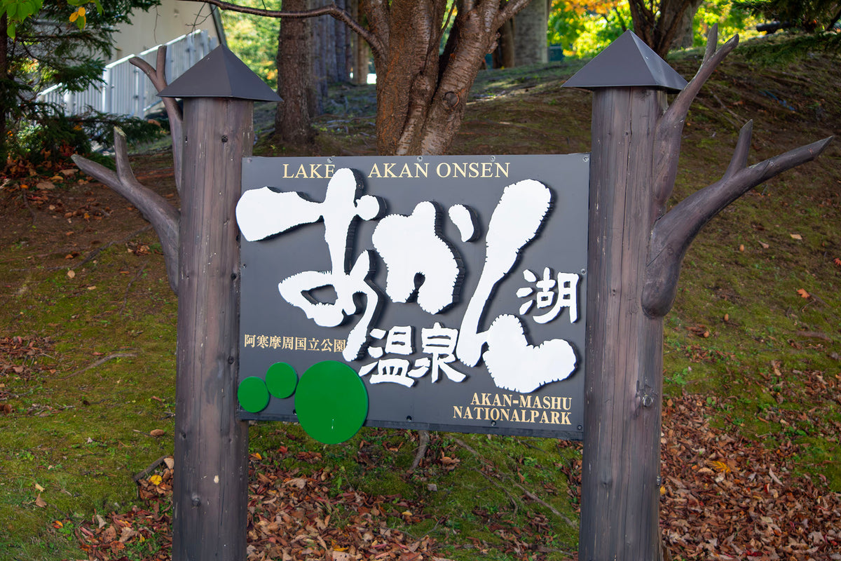 Sign for Lake Akan Onsen at Akan-Mashu National Park, featuring three stylized green marimo moss balls, symbolizing the region’s natural pride and cultural identity.