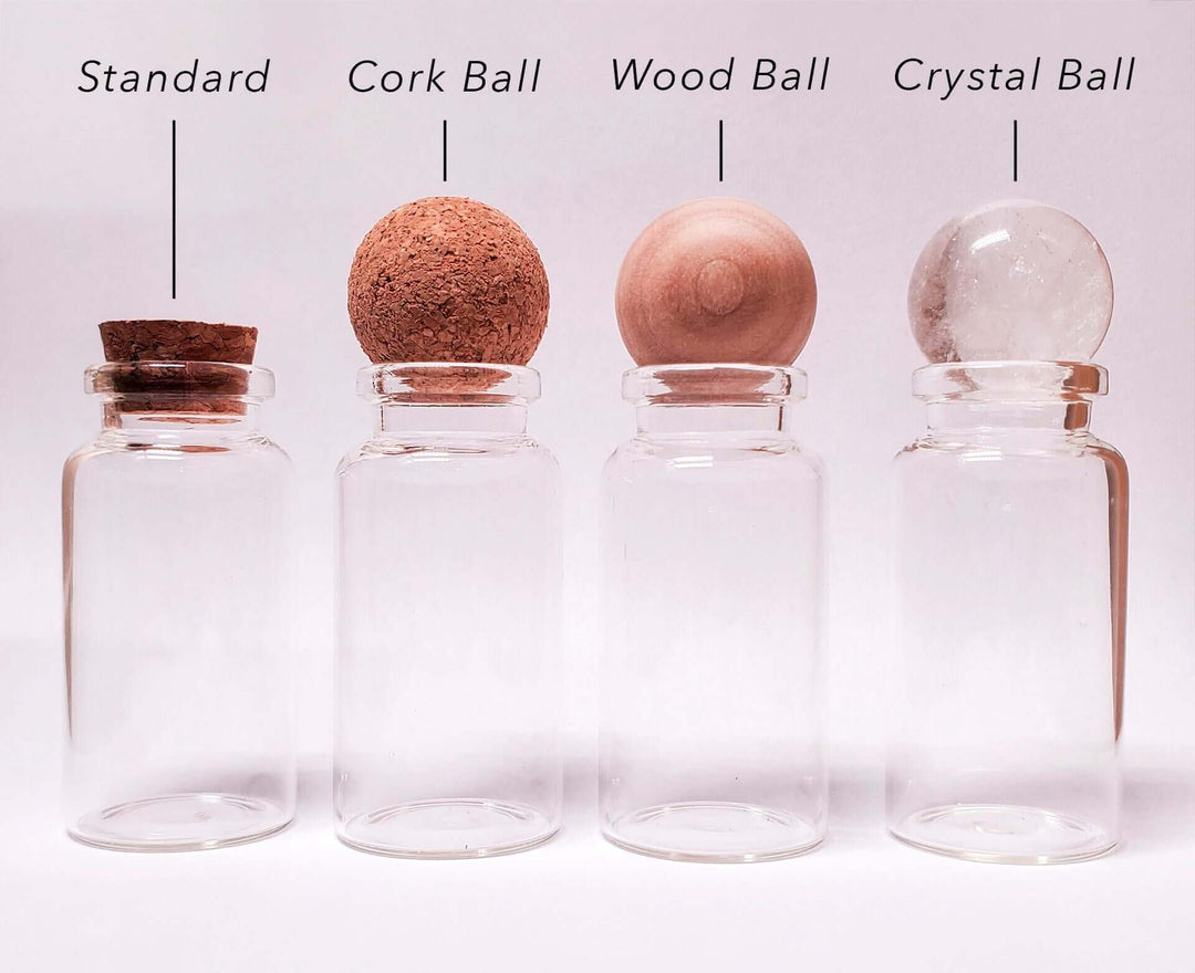 A lineup of bottle toppers including a standard cork, a textured cork ball, a smooth wood ball, and a crystal ball against a white background.