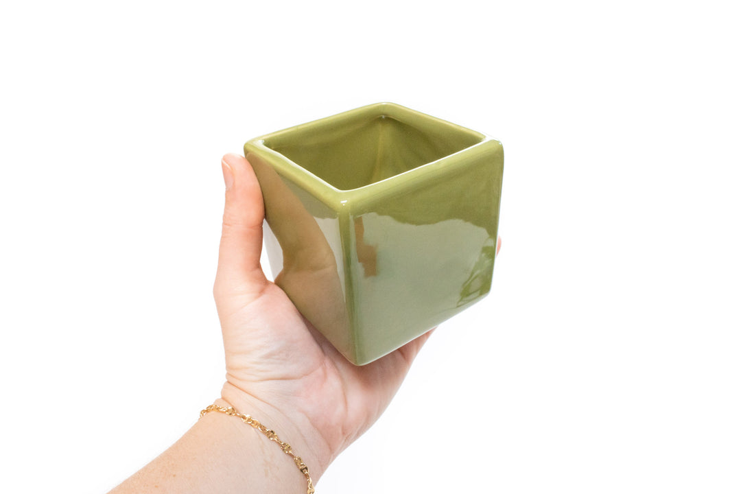 Hand holding an empty olive green ceramic cube container