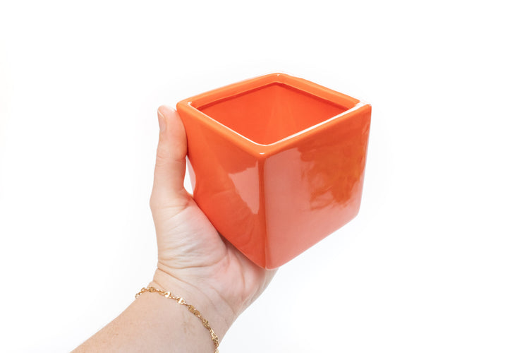 Hand holding an empty orange ceramic cube container