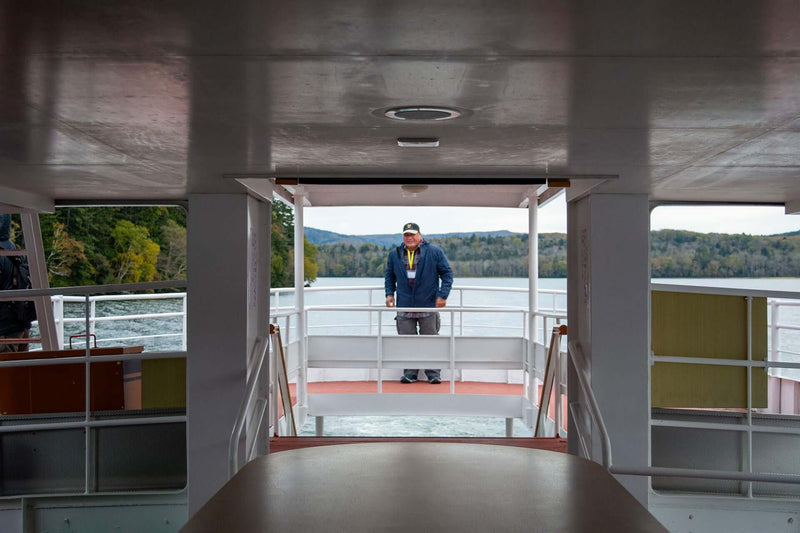 A tourist is framed in the open hallway of the ferry with Lake Akan and forested hills in the background.