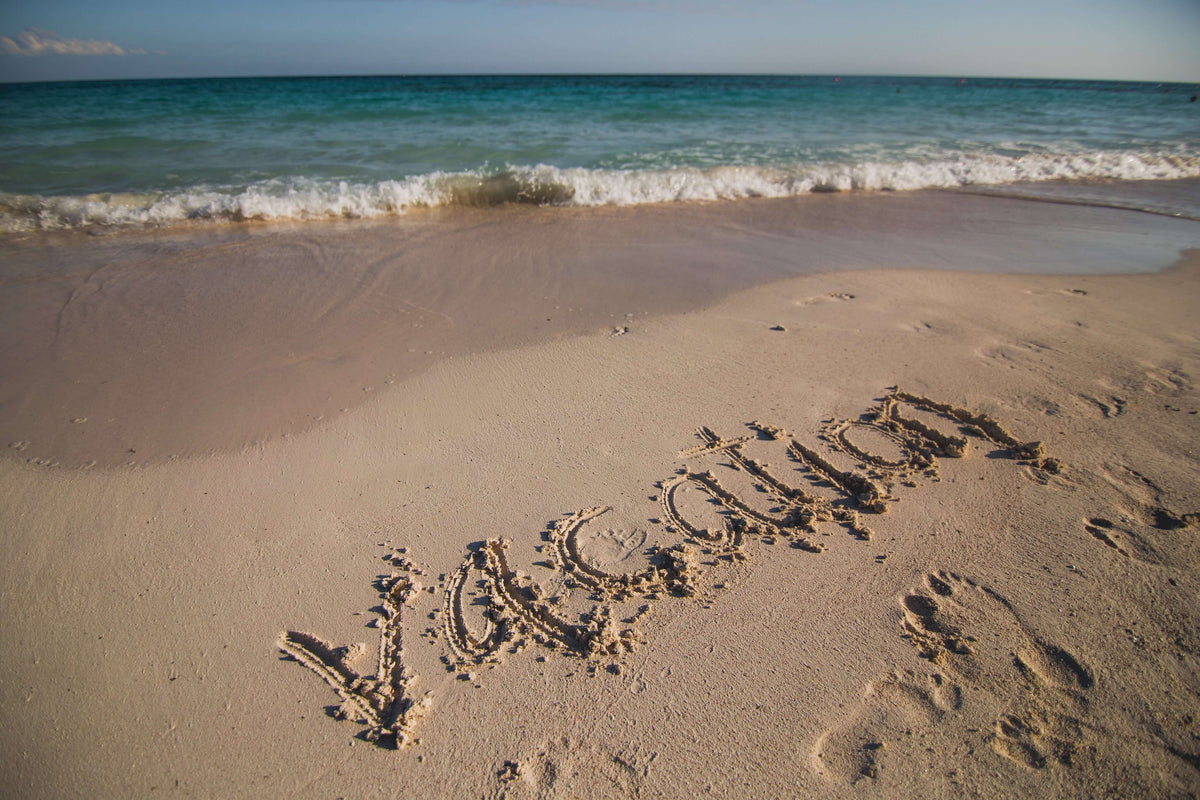 Vacation written in the sand on a beach, a reminder to plan class pet care over breaks